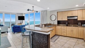 A modern kitchen with a large island, wooden cabinets, and a view of the ocean.