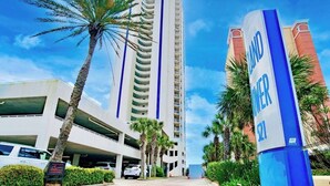 A tall hotel with a prominent blue and white sign, a parking garage, and palm trees.