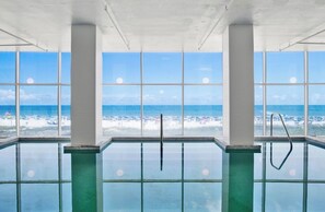 Una piscina interior con amplias ventanas que ofrecen vista a la playa y al océano.