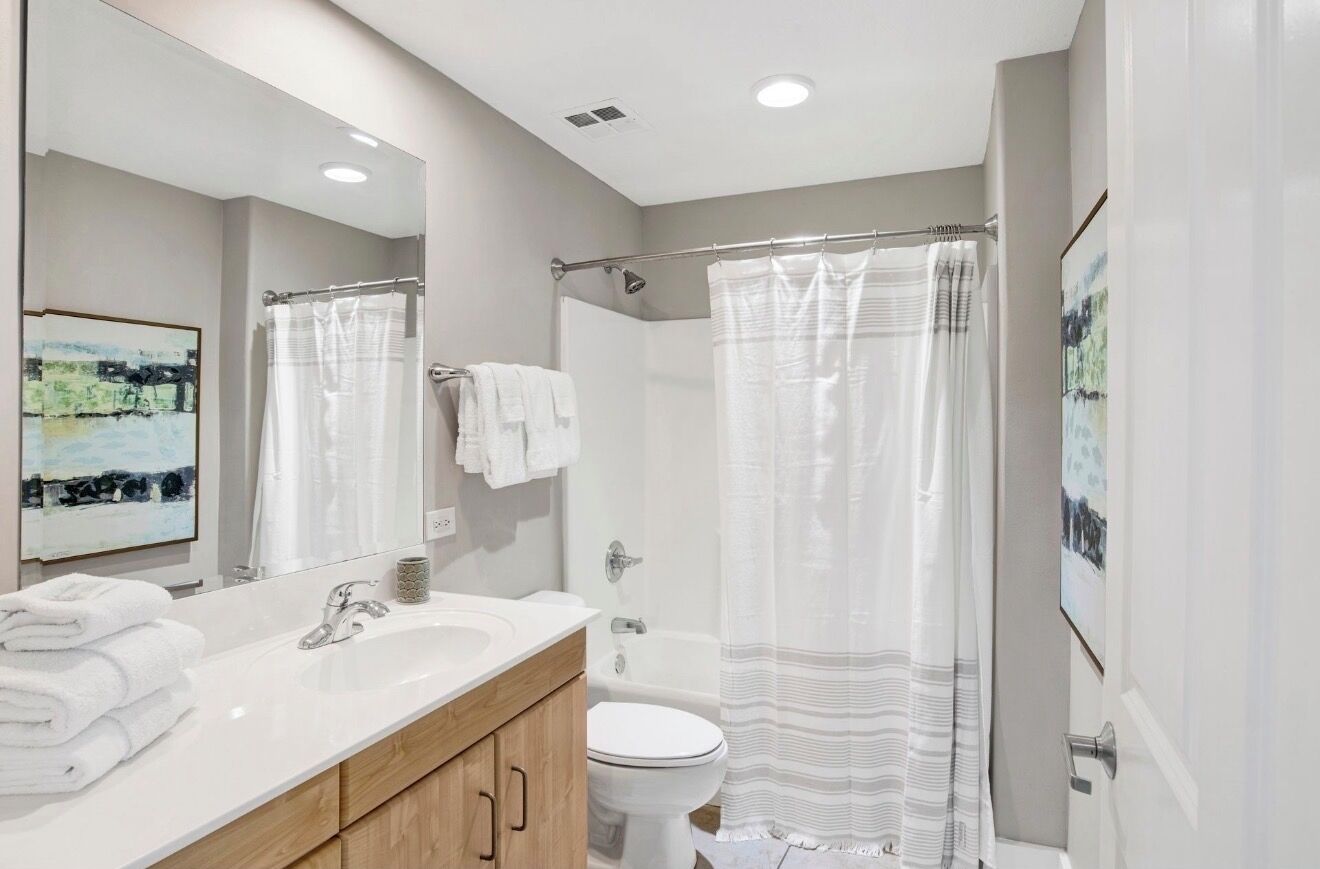 Un baño moderno con un espejo grande, un lavabo blanco y una cortina de ducha.