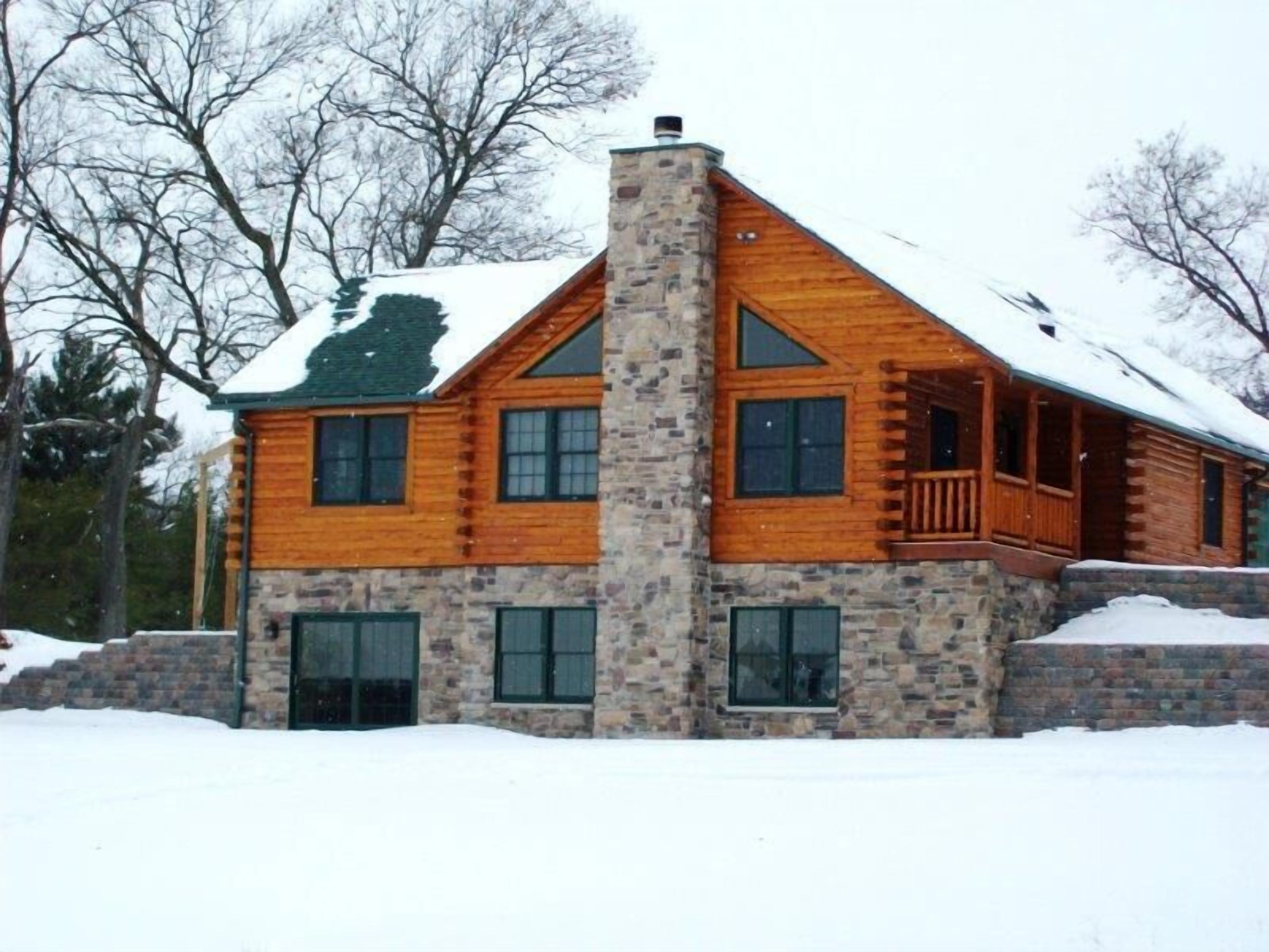 A log cabin with a stone chimney, multiple windows, and a balcony.