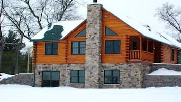 A log cabin with a stone chimney, multiple windows, and a balcony.