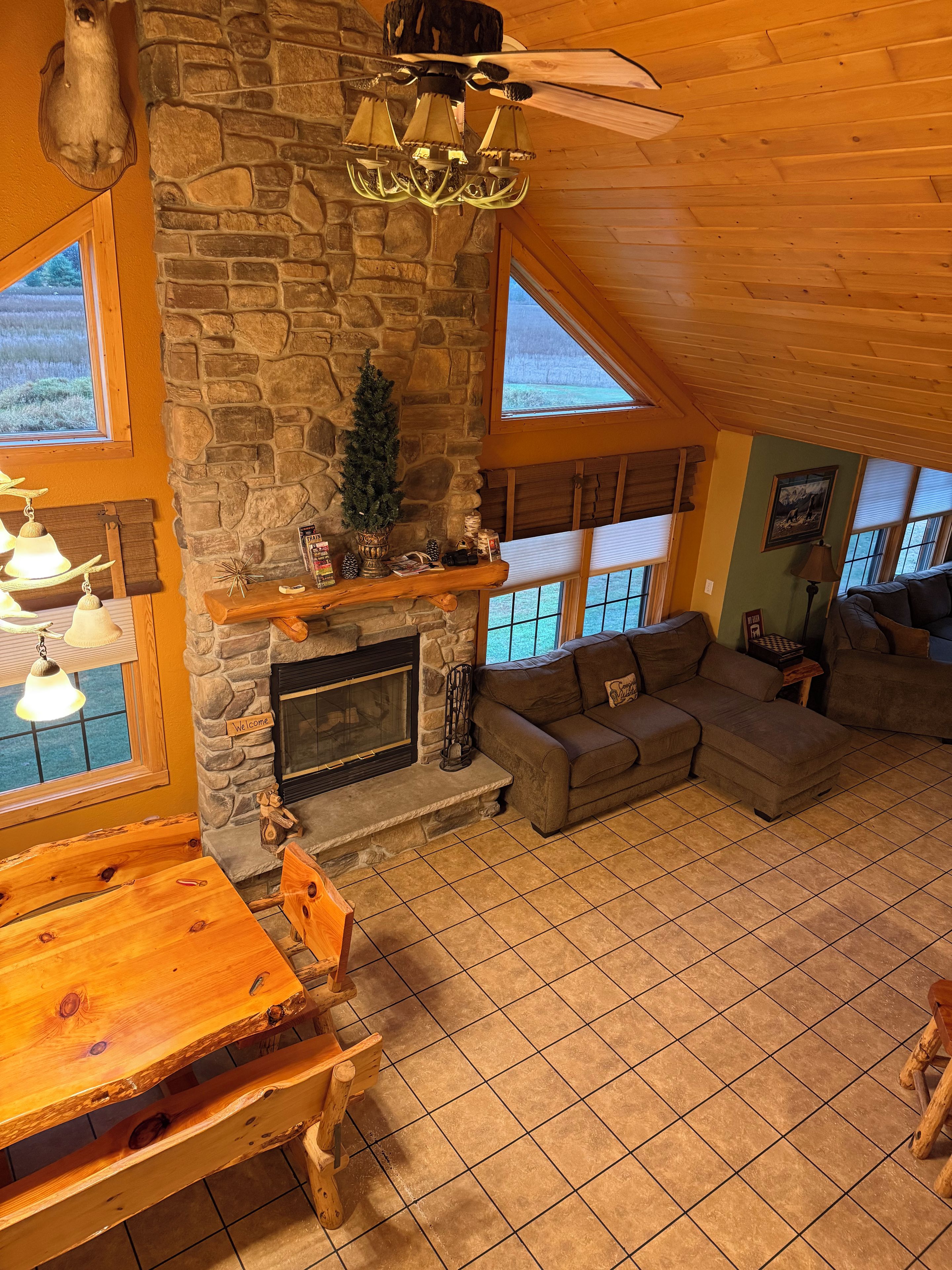 A cozy interior with a stone fireplace, wooden furniture, and large windows.