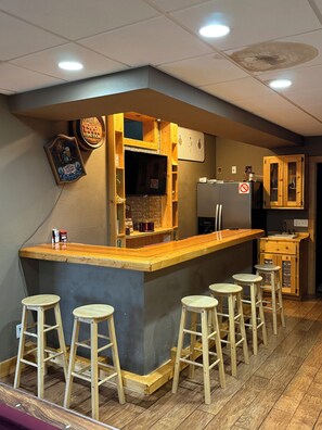 A bar area with stools, a refrigerator, and wooden cabinets.