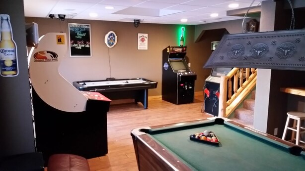 Een pooltafel met een keu, een biljarttafel en een neonverlichte speelautomaat.