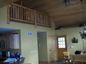 Une pièce spacieuse avec un plafond en bois, un coin cuisine équipé de placards et d’un évier, une porte en bois et une petite fenêtre.