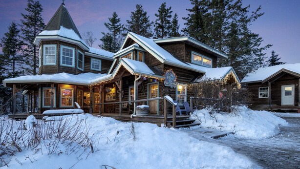 Une cabane en rondins dont l’extérieur est recouvert de neige, une véranda avec des sièges d’extérieur et une enseigne de librairie bien visible.