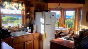 Une cuisine avec des meubles de rangement en bois, un réfrigérateur blanc, un évier et une fenêtre donnant sur un paysage verdoyant.