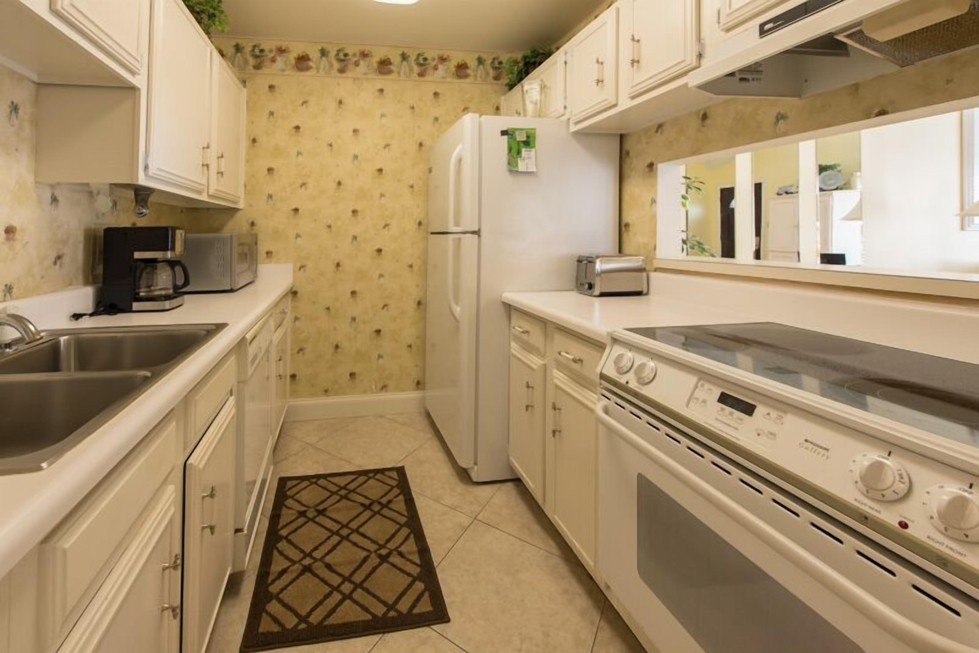A compact kitchen with white cabinets, a refrigerator, a microwave, a toaster, and a stove.