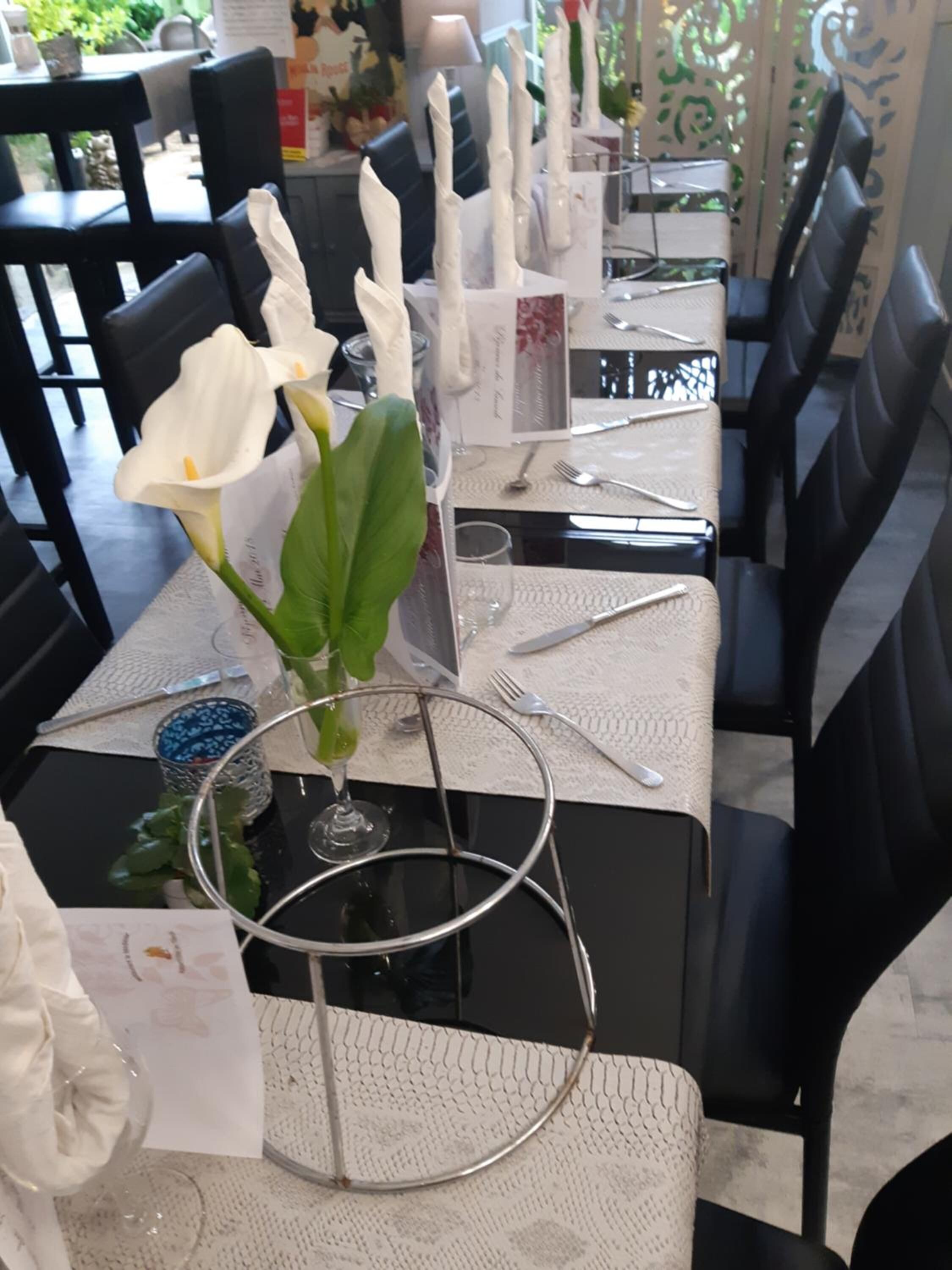 A dining table set with white napkins, a vase with white flowers, and a metal ring.