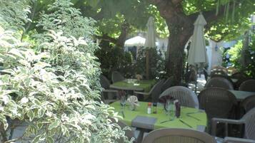 An outdoor dining area with tables and chairs, surrounded by greenery and trees.