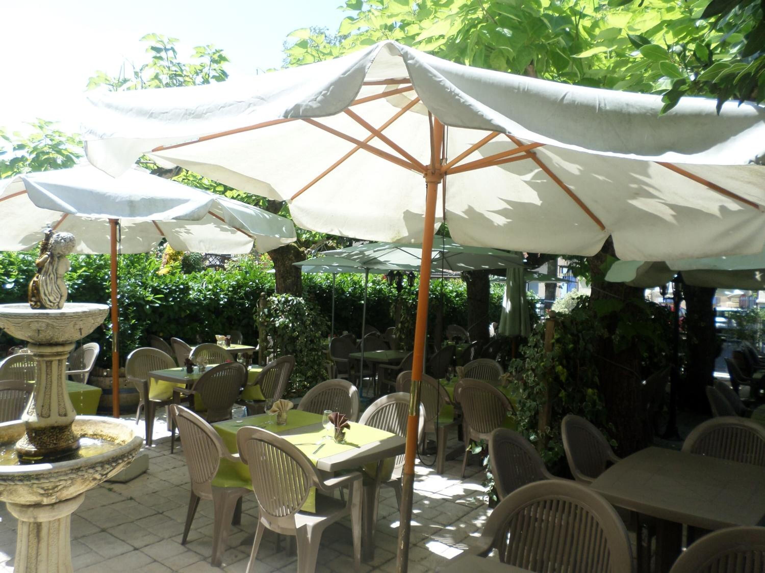 An outdoor patio area with tables and chairs, umbrellas, and a decorative fountain.