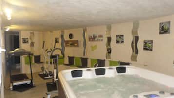 A room with a large hot tub, exercise equipment, and a wall with various pictures.