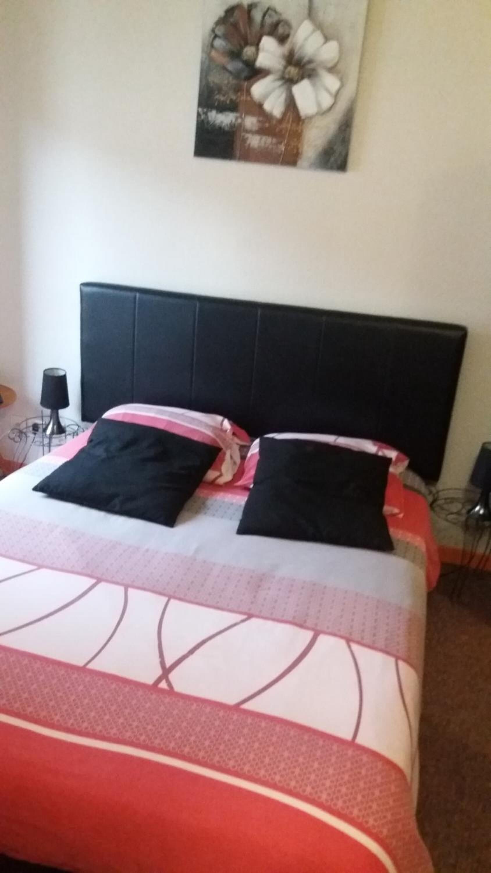 Una cama con cabecera negra, dos almohadas negras y una colcha estampada.