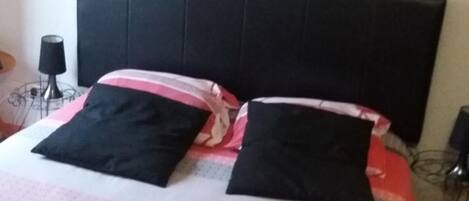 Una cama con cabecera negra, dos almohadas negras y una colcha estampada.