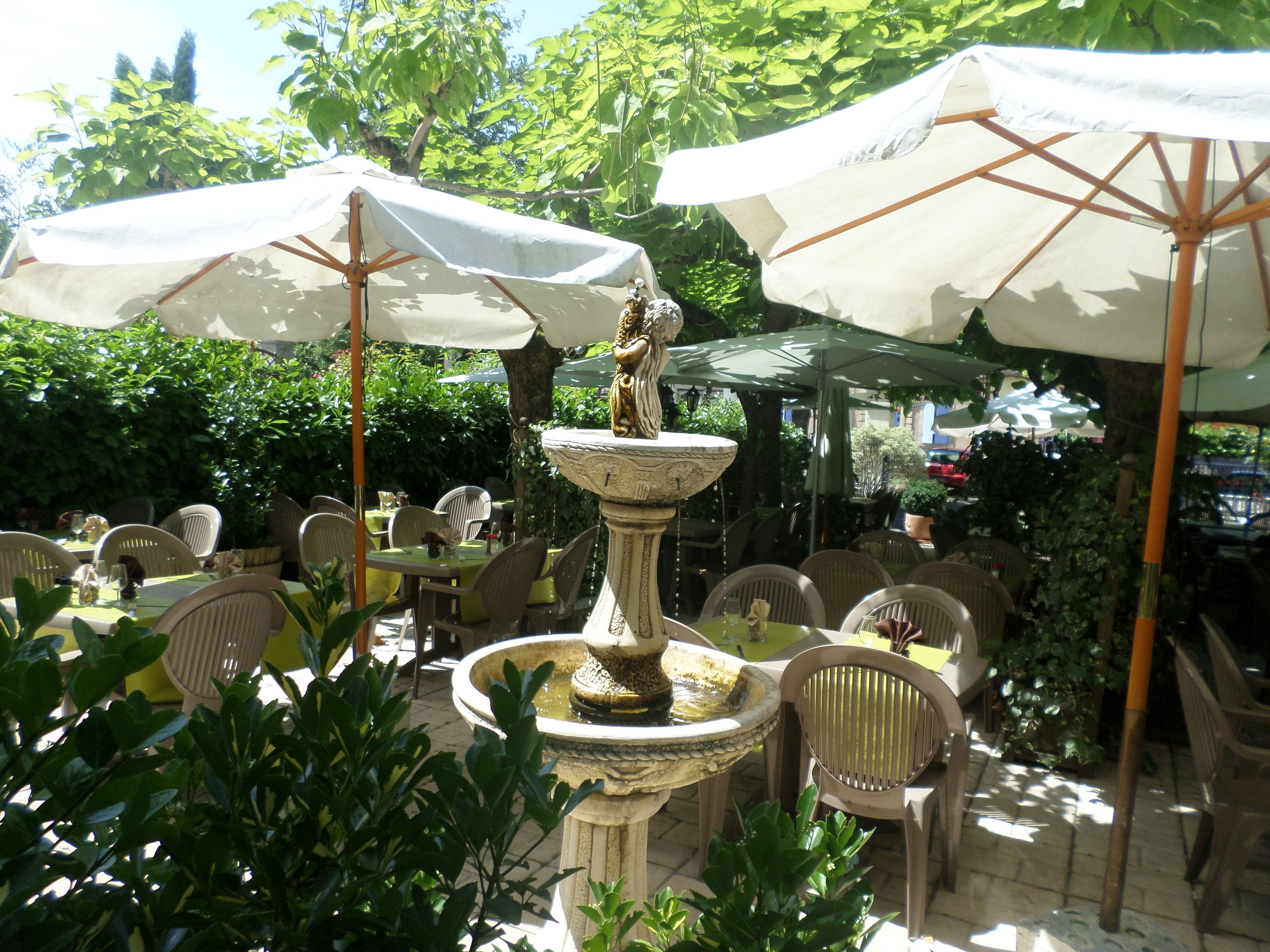 An outdoor dining area with tables and chairs, umbrellas, and a central fountain.