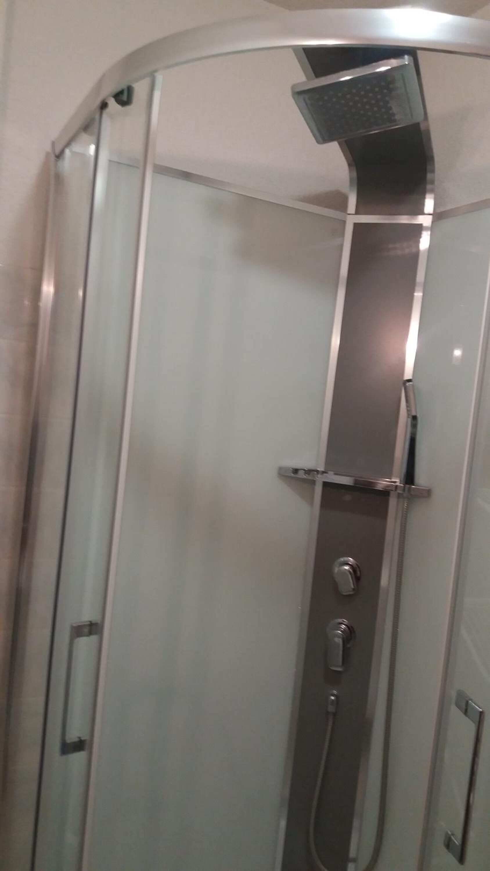 A glass-enclosed shower stall with a handheld showerhead and a handheld faucet.