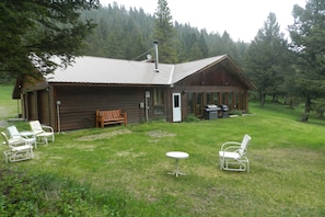 Eine rustikale Holzhütte mit einem Metalldach, einer Holztür und einer kleinen Veranda mit einer Bank und zwei Stühlen.