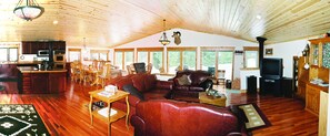 Ein geräumiges Wohnzimmer mit Holzbalkendecke, Kamin, Fernseher und Essbereich mit Holzmöbeln.