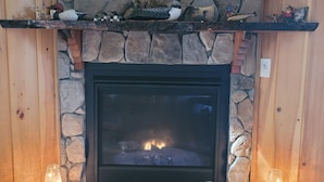 A stone fireplace with a black hearth, flanked by wooden mantels and two lit candles. - Balsam Point Lakehouse · Indian Lake Adirondacks · Waterfront on Lake Abanakee (Indian Lake)