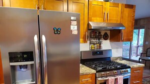 A kitchen with stainless steel appliances, wooden cabinets, a water dispenser, and a gas stove. - Balsam Point Lakehouse · Indian Lake Adirondacks · Waterfront on Lake Abanakee (Indian Lake)