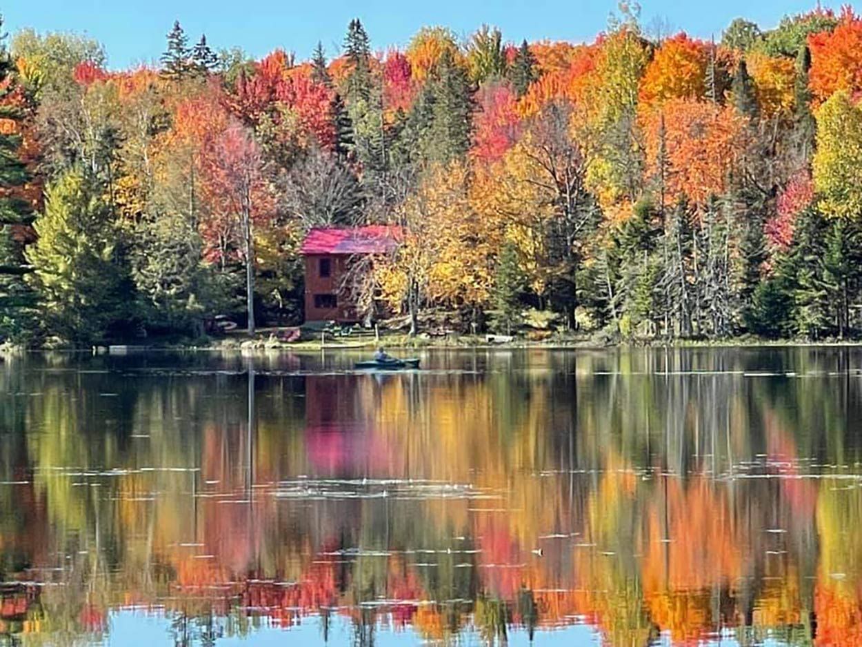 Un lago con el reflejo de árboles coloridos y un edificio de techo rojo.
