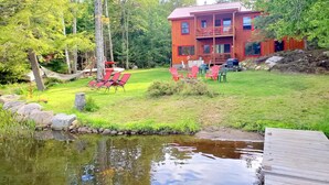 A wooden cabin with a deck and outdoor seating, surrounded by a pond and forest. - Balsam Point Lakehouse · Indian Lake Adirondacks · Waterfront on Lake Abanakee (Indian Lake)