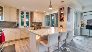A modern kitchen with a central island, bar stools, and a large window providing natural light.