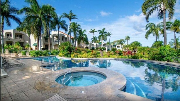 A resort pool area with a hot tub, palm trees, and a building with balconies.