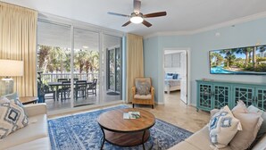 A spacious living area with a large sliding glass door leading to an outdoor patio, a ceiling fan, a television mounted on the wall, and a cozy seating arrangement with a coffee table.