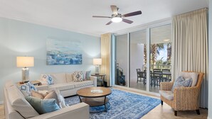 A modern living room with a sofa, coffee table, and armchair, a ceiling fan, and a large sliding glass door leading to an outdoor patio.
