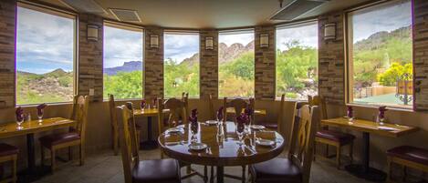 A dining area with a large round table and chairs, large windows with a view of a mountainous landscape.