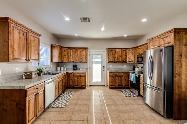 A modern kitchen with wooden cabinets, stainless steel appliances, and a tiled floor.
