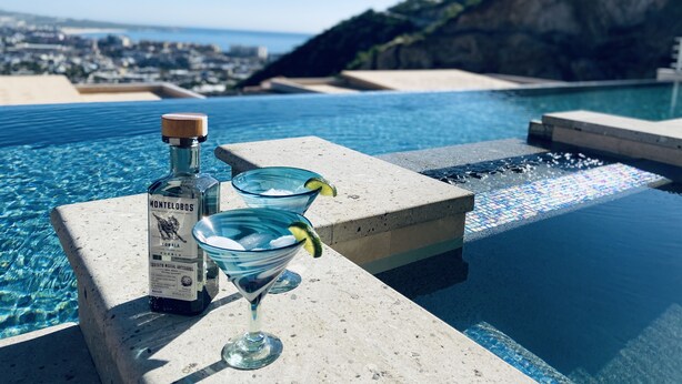 A poolside setting with a bottle of Montecristo tequila, a martini glass, and a cocktail glass with a lime garnish. - Luxury w/ Breathtaking Views! 10-minute walk to the marina - Cascadas 302 (Cabo San Lucas)