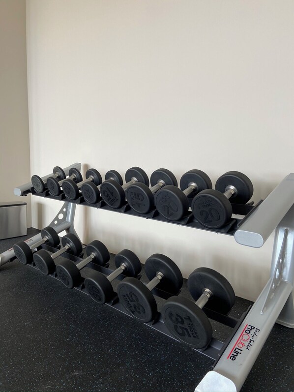 A set of dumbbells on a rack with weight markings, a stainless steel dumbbell, and a black countertop.