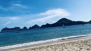 A beach with a cruise ship, boats, and a mountainous backdrop. - Luxury w/ Breathtaking Views! 10-minute walk to the marina - Cascadas 302 (Cabo San Lucas)
