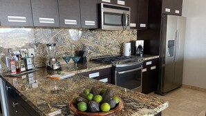A modern kitchen with granite countertops, stainless steel appliances, and a bowl of avocados. - Luxury w/ Breathtaking Views! 10-minute walk to the marina - Cascadas 302 (Cabo San Lucas)