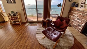 Ein Wohnzimmer mit Ledersofa, Kamin und Meerblick durch große Schiebetüren.