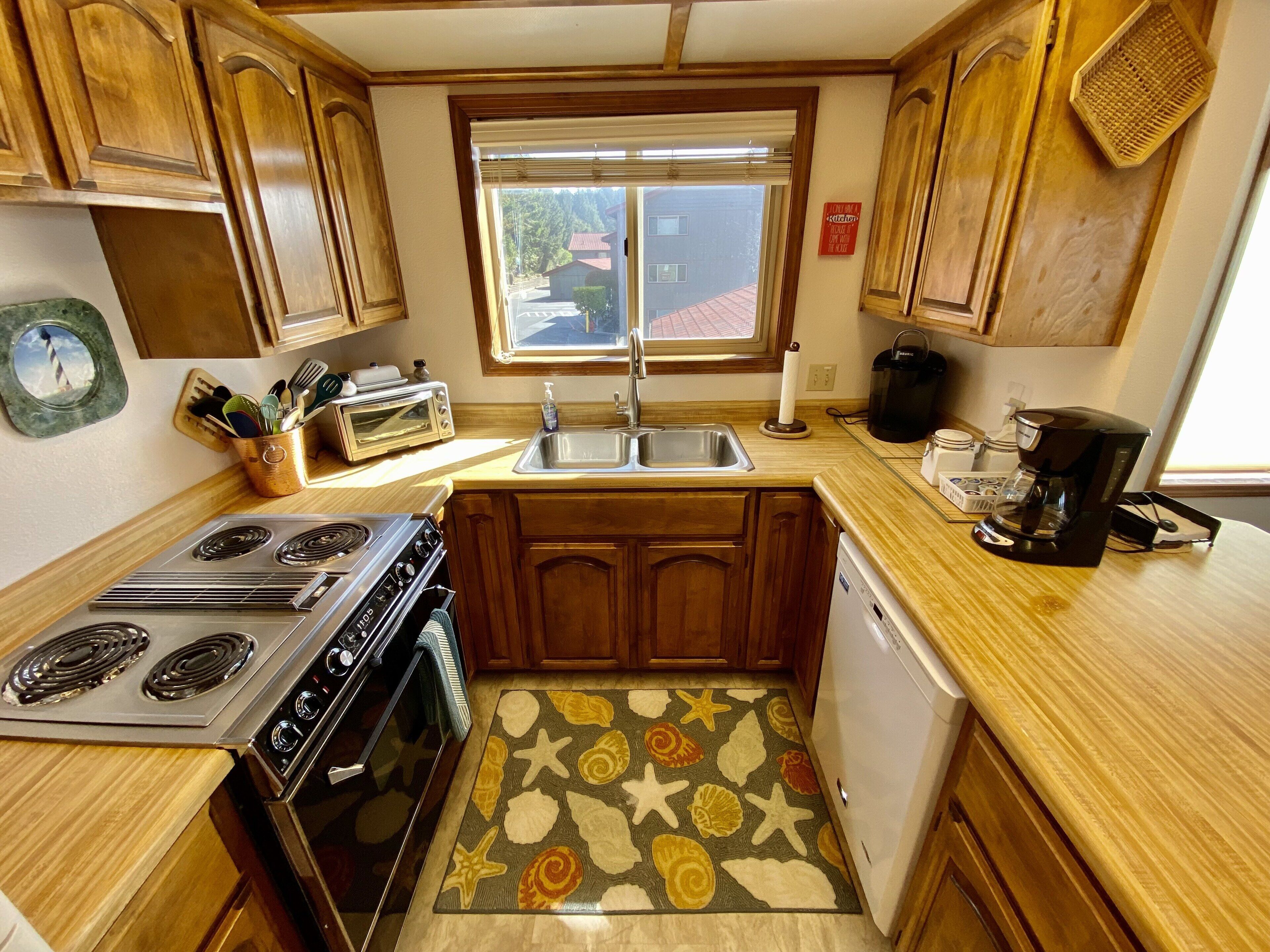 A compact kitchen with wooden cabinets, a built-in oven, a stovetop, a sink, and a coffee maker.
