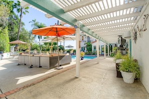 A covered outdoor area with a pool, lounge chairs, and umbrellas.