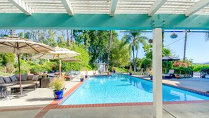 Une piscine dotée d’une terrasse carrelée, entourée de mobilier de jardin et de parasols.