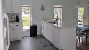 Uma cozinha moderna com armários brancos, uma ilha grande e vista para o exterior.
