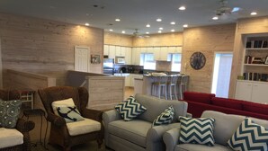 A living room with a grey sofa, wicker chairs, and a red couch. A kitchen with white cabinets and a microwave is visible in the background. - Close to the beach. Spacious & bright with gorgeous views from 3rd decks. (Galveston)