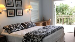 A bedroom with a bed, bedside lamps, a desk, and a view of a balcony with plants. - Close to the beach. Spacious & bright with gorgeous views from 3rd decks. (Galveston)