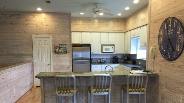 A kitchen with wooden walls, a stainless steel refrigerator, a microwave, a sink, and a clock on the wall. - Close to the beach. Spacious & bright with gorgeous views from 3rd decks. (Galveston)