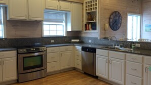 A modern kitchen with white cabinets, stainless steel appliances, a granite countertop, and a wooden floor. - Close to the beach. Spacious & bright with gorgeous views from 3rd decks. (Galveston)