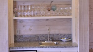 A kitchen with a built-in dishwasher, a sink, and a wooden shelf unit with glassware and decorative items. - Close to the beach. Spacious & bright with gorgeous views from 3rd decks. (Galveston)