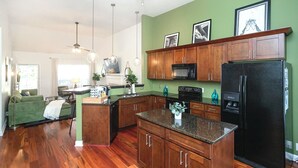 Een moderne keuken met houten kasten, een zwarte koelkast en een eethoek met een groene bank.