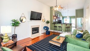 Een moderne woonkamer met een open haard, een groene bank en een keukenhoek met barstoelen.