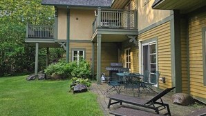 Ein zweistöckiges Haus mit überdachter Terrasse, Grill und Gartenmöbeln.